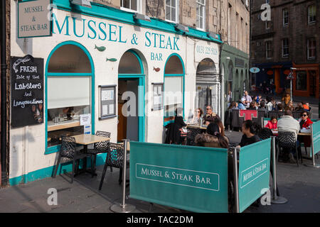 Customers sitting outside the Mussel and Steak Bar, a surf and turf restaurant in West Bow, Grassmarket,  Edinburgh, Scotland. Clients of Auld Jock's  Stock Photo
