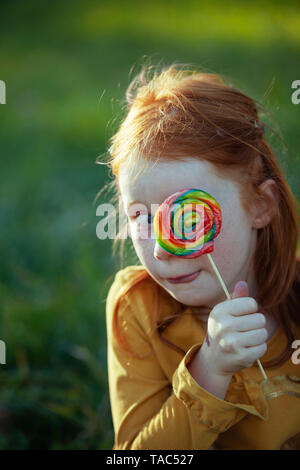 Grimacing girl covering her eye with a lollipop Stock Photo