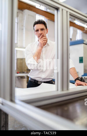 Man wearing white shirt in factory thinking Stock Photo