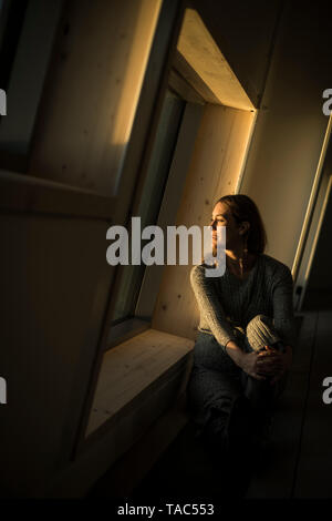 Woman sitting at office window at sunset, portrait Stock Photo