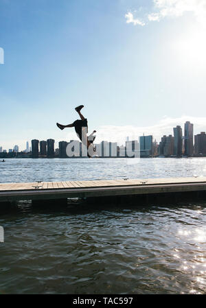 USA, New York, Brooklyn, young man doing backflip on pier in front of Manhattan skyline Stock Photo