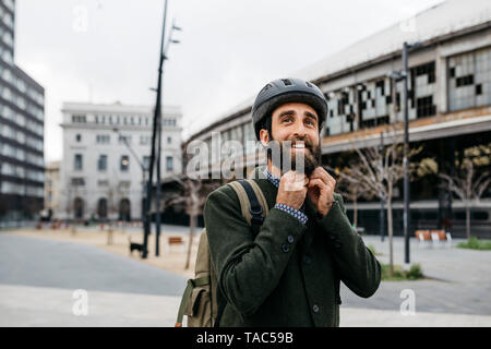 Portrait of smiling man putting on bicycle helmet in the city