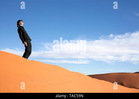 Morocco, Merzouga, Erg Chebbi, man wearing a bowler hat standing crooked on desert dune Stock Photo