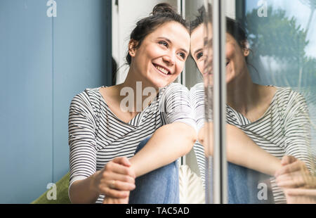 Smiling woman looking out of window at home Stock Photo