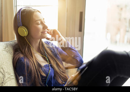 Relaxed young woman sitting on a chair wearing headphones Stock Photo