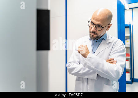 Man wearing lab coat and glasses looking at machine Stock Photo