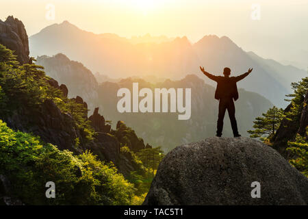 Hiker is standing on a rock with raised hands and enjoying sunrise Stock Photo