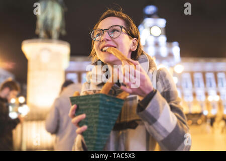 Spain, Madrid, young woman in the city at night eating typical churros with chocolate Stock Photo