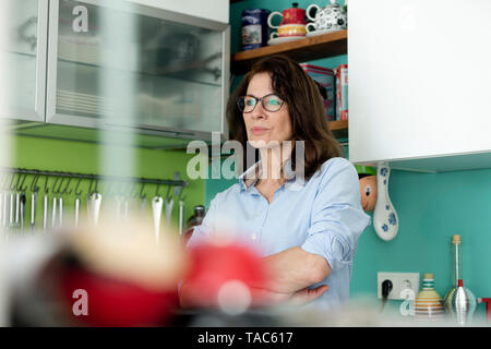 Portrait of pensive mature woman in kitchen at home Stock Photo