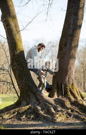 Father playing with son at a tree in park Stock Photo