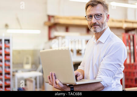 Portrait of confident businessman using laptop in factory Stock Photo
