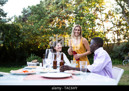 Friends at a summer dinner in the garden opening bottle of wine Stock Photo