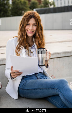 Young businesswoman sitting on stairs in the city, reading document Stock Photo