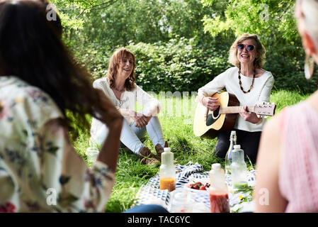 Group of women with guitar having fun at a picnic in park Stock Photo