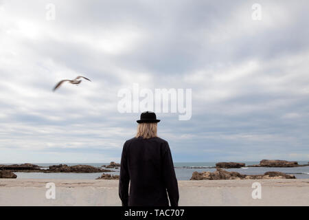 Morocco, Essaouira, rear view of man wearing a bowler hat standing at the sea