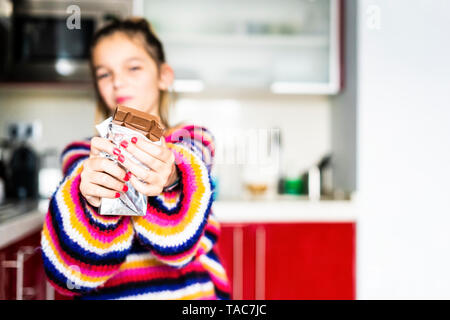 Girl in striped pullover in kitchen at home eating chocolate Stock Photo