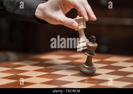 Concept: the woman who dominates the man. A woman's hand gives checkmate to  the king with the queen on a wooden chessboard, with no other pieces in  play Stock Photo