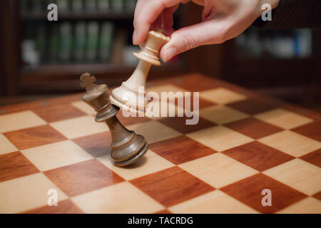 Concept: the woman who dominates the man. A woman's hand gives checkmate to  the king with the queen on a wooden chessboard, with no other pieces in  play Stock Photo