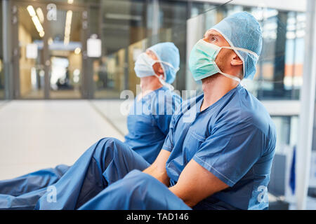 Two exhausted surgeons in blue surgical clothing as a sign of stress and fatigue Stock Photo