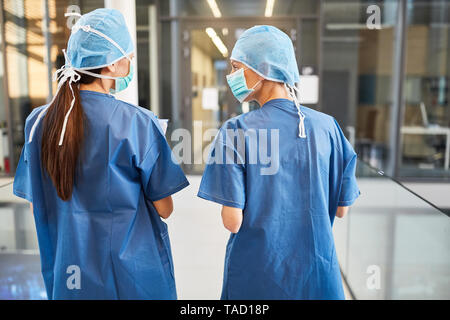 Two young women as surgeons in blue surgical clothing talking in the emergency room Stock Photo
