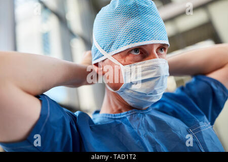 Surgeon in blue surgical gown with surgical mask and hood prepared for emergency service Stock Photo