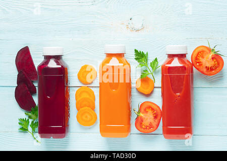 Fresh juice smoothies from a variety of vegetables carrots apple tomatoes beets in bottles on a wooden blue background. Stock Photo