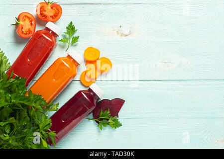 Fresh juice smoothies from a variety of vegetables carrots apple tomatoes beets in bottles on a wooden blue background. Stock Photo