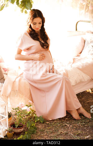 Beautiful pregnant woman posing outdoors. Holding pregnant tummy. Maternity. 20s. Stock Photo