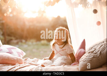 Smiling baby girl 1-2 year old wearing stylish dress sitting in bed outdoors. Happy birthday. Childhood. Stock Photo
