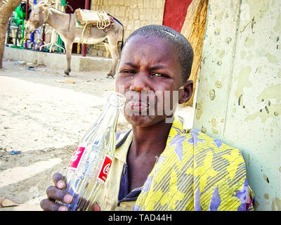 TIMBUKTU, MALI - FEBRUARY Circa, 2019. Unidentified poor child is drinking a coca-cola bottle, given by tourist in street of village in Mali Stock Photo