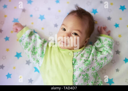 Close-up portrait of baby girl laying on bed in sunny day Stock Photo