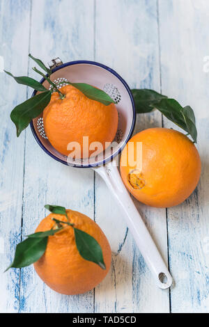 Three oranges with leaves and a colander on wood Stock Photo