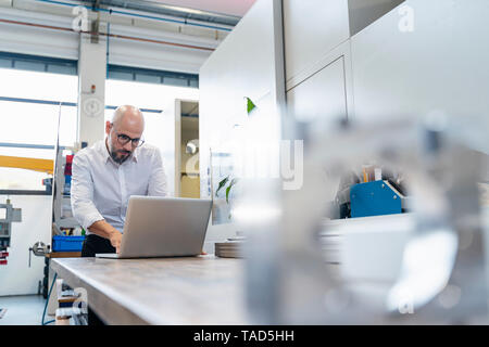 Focused businessman using laptop in factory Stock Photo