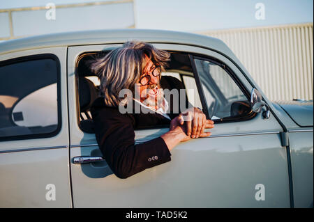 Senior man leaning out of window of vintage car screaming Stock Photo