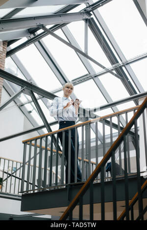 Businesswoman standing in loft office, using smartphone Stock Photo