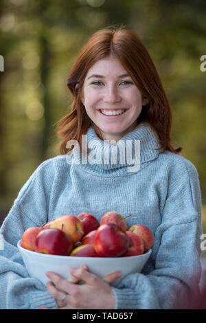 Portrait of happy redheaded teenage girl holding bowl of apples Stock Photo