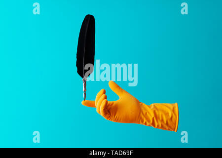 Quill pen balancing in a hand over cyan background Stock Photo