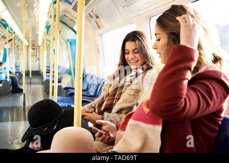 UK, London, two happy women in underground train using cell phone