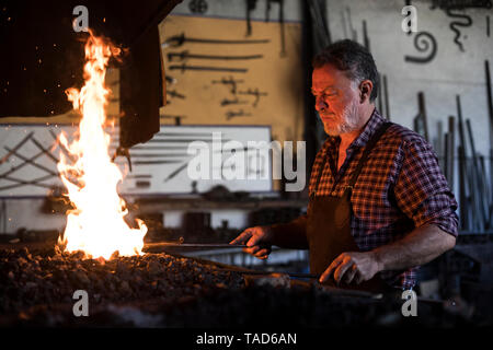 Blacksmith working at forge in his workshop Stock Photo