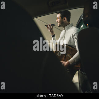 Smiling young man with bag using cell phone at a car Stock Photo