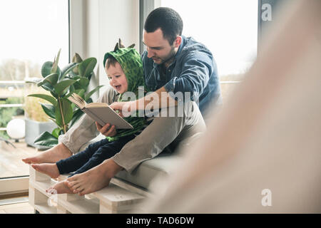 Boy in a costume with father reading book at home Stock Photo