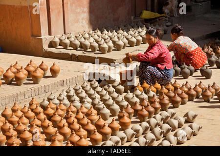 Women dipping pottery into color as other clay products sun-dry near Kumale Tol (Potters' Square, Pottery Square),  Bhaktapur, Kathmandu Valley, Nepal Stock Photo