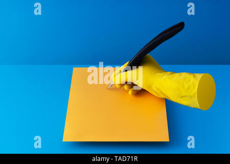 Quill pen held in hand and writing on orange paper over blue background Stock Photo