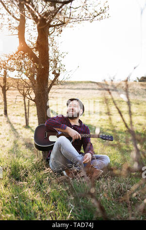 Man playing guitar at a tree on a meadow Stock Photo