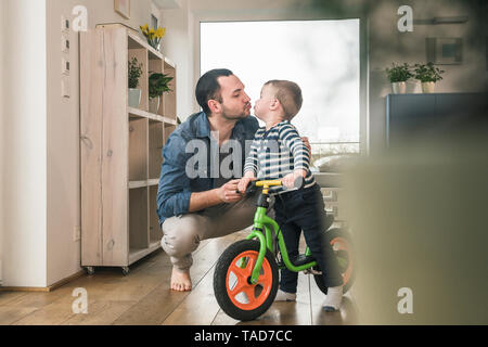 Father kissing son with a balance bicycle at home Stock Photo