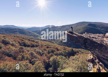 Spain, Navarra, Irati Forest, woman sitting on rock spur above forest landscape in backlight Stock Photo