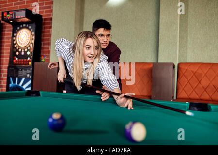Young man guiding girlfriend at billiard table Stock Photo