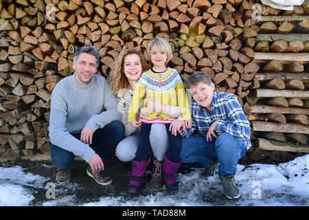 Portrait of happy family in front of stack of wood in winter Stock Photo