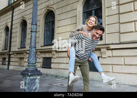 Happy man giving woman piggyback ride on pavement in the city Stock Photo