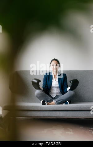 Portrait of young woman sitting on couch wearing boxing gloves Stock Photo